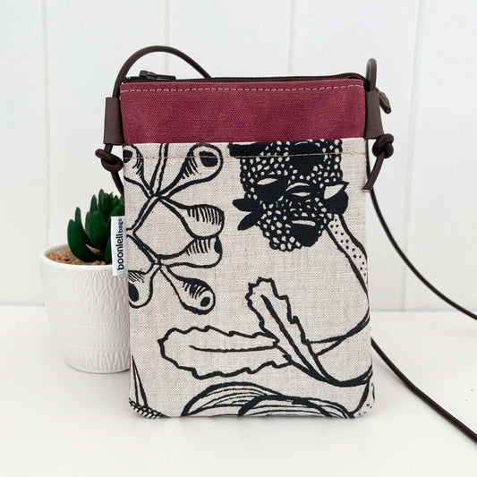 A small crossbody bag with a black and white botanical print on a linen-textured base, featuring a dusty rose top panel and dark brown straps. A small white tag on the side reads 'bookishbag'.