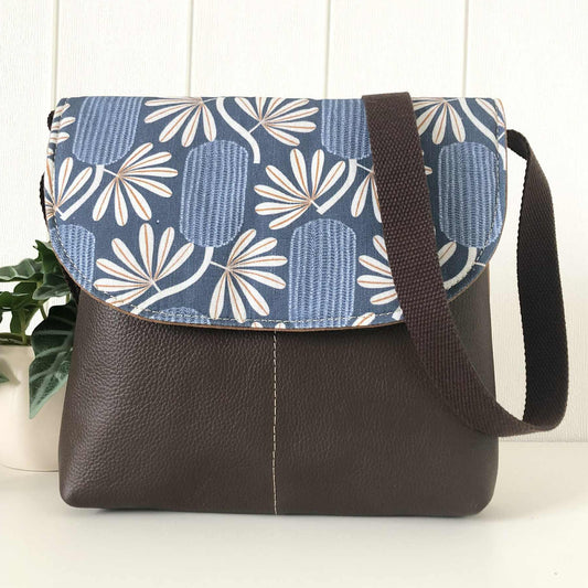 Crossbody bag with blue floral patterned flap and brown leather body on a white background