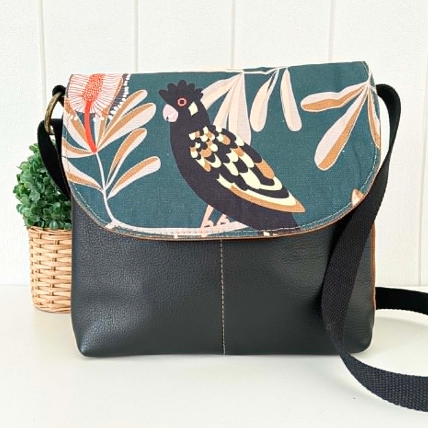 Black shoulder bag with bird and leaf pattern on flap, placed against a white background.