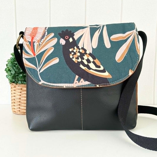 Black shoulder bag with bird and leaf pattern on flap, placed against a white background.