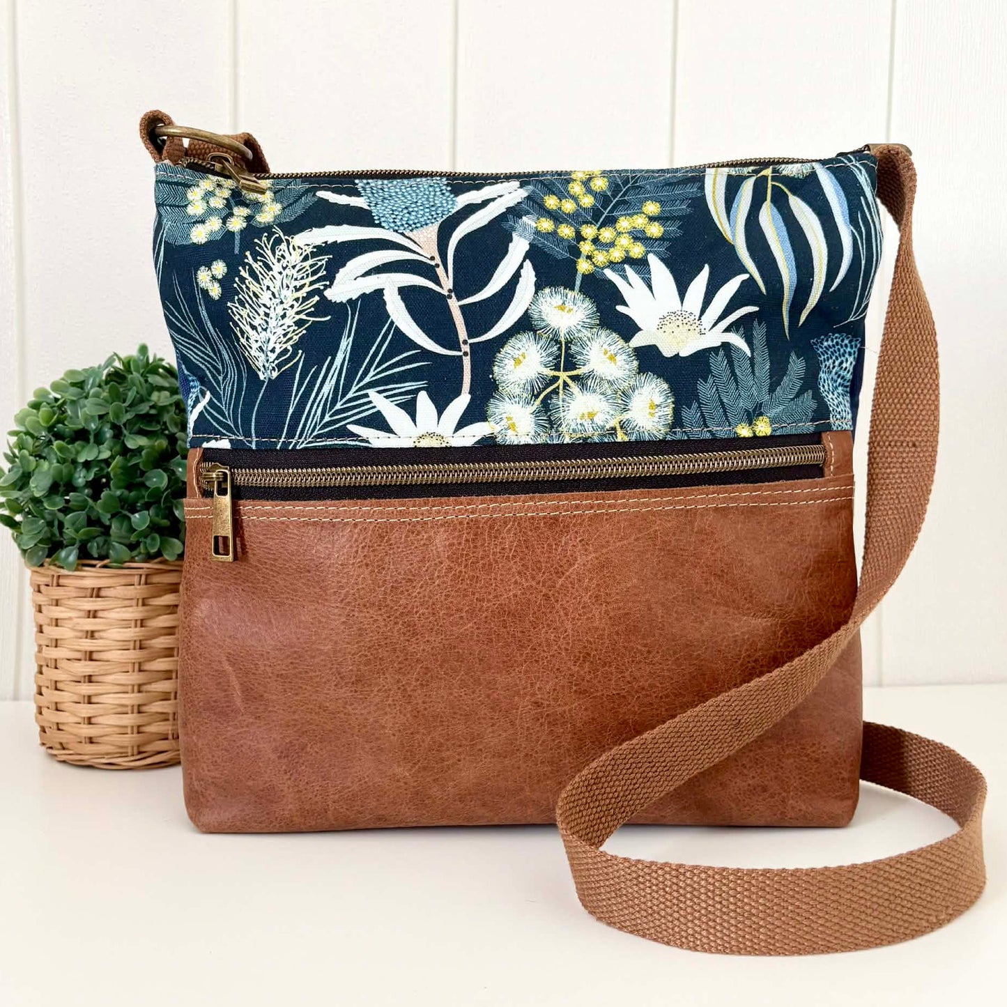 Crossbody bag with floral patterned top section and brown leather bottom section on a white background