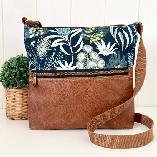 Crossbody bag with floral patterned top section and brown leather bottom section on a white background