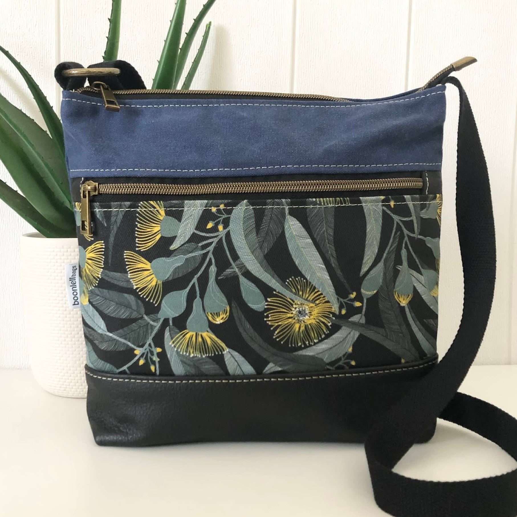 Floral-patterned crossbody bag with a blue top section on a white surface.