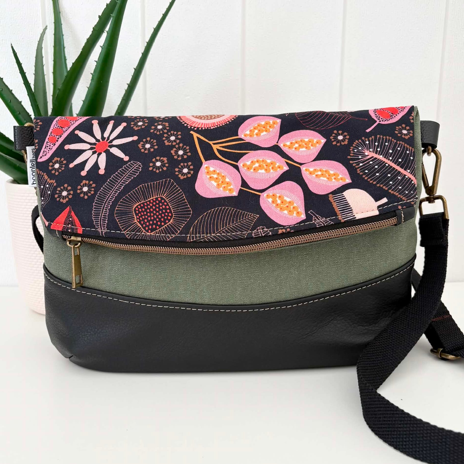 Floral patterned handbag with a black strap on a white surface