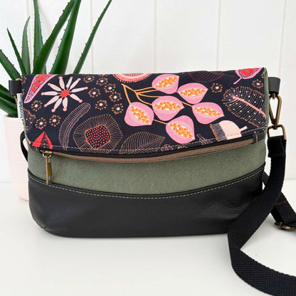 Floral patterned handbag with a black strap on a white surface