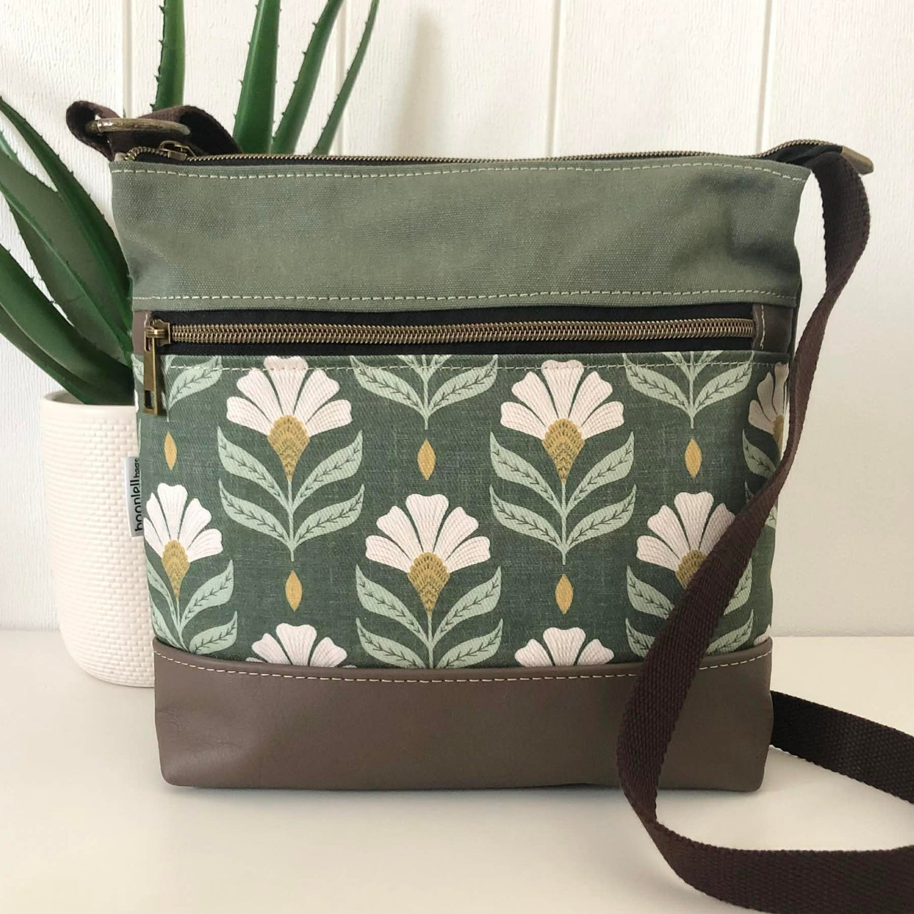 Green floral-patterned bag with a brown strap on a white surface.