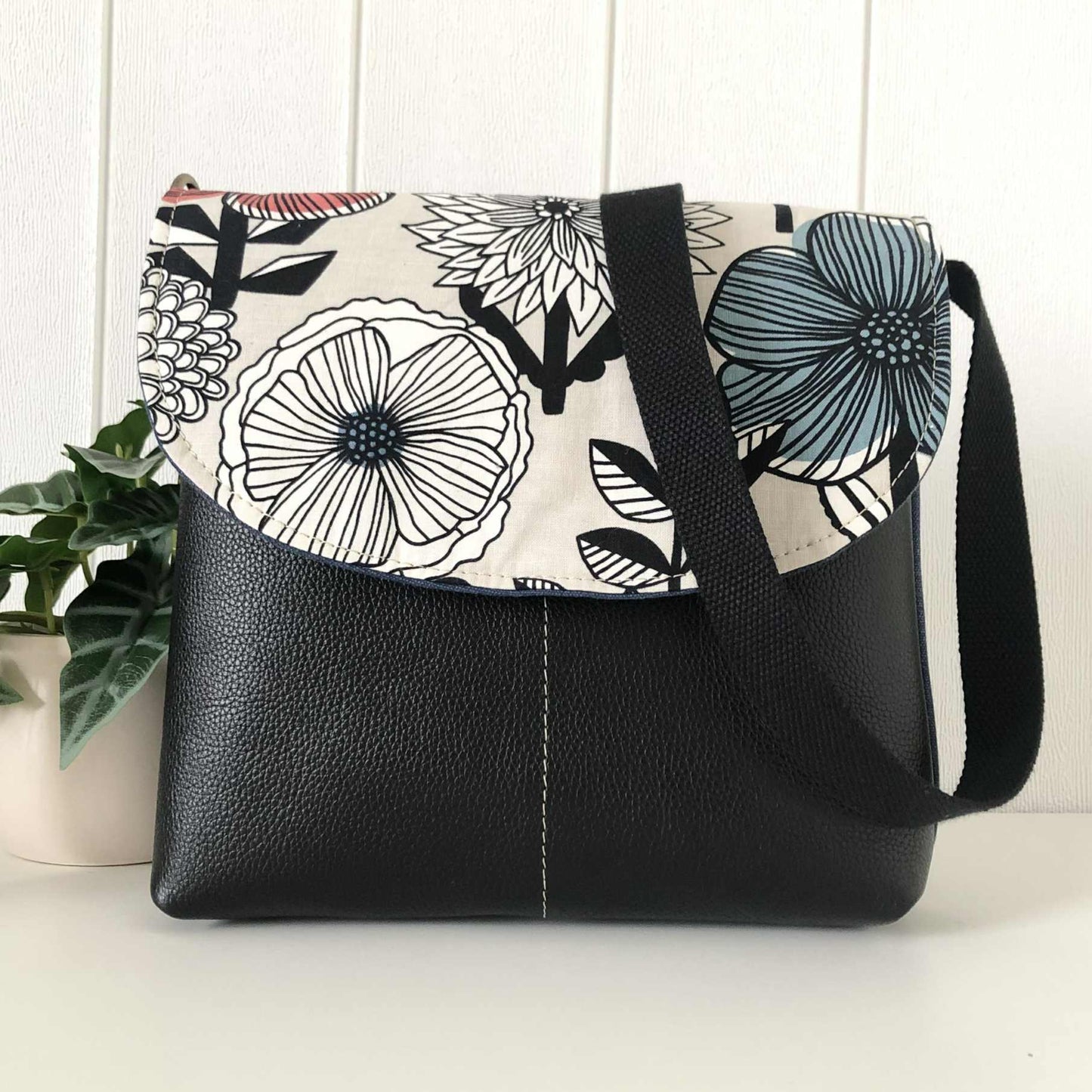 Black handbag with floral patterned flap on a white surface