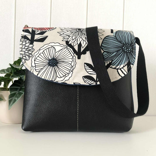 Black handbag with floral patterned flap on a white surface