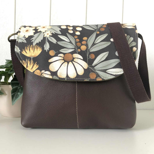 Floral-patterned bag with brown leather flap on a white surface