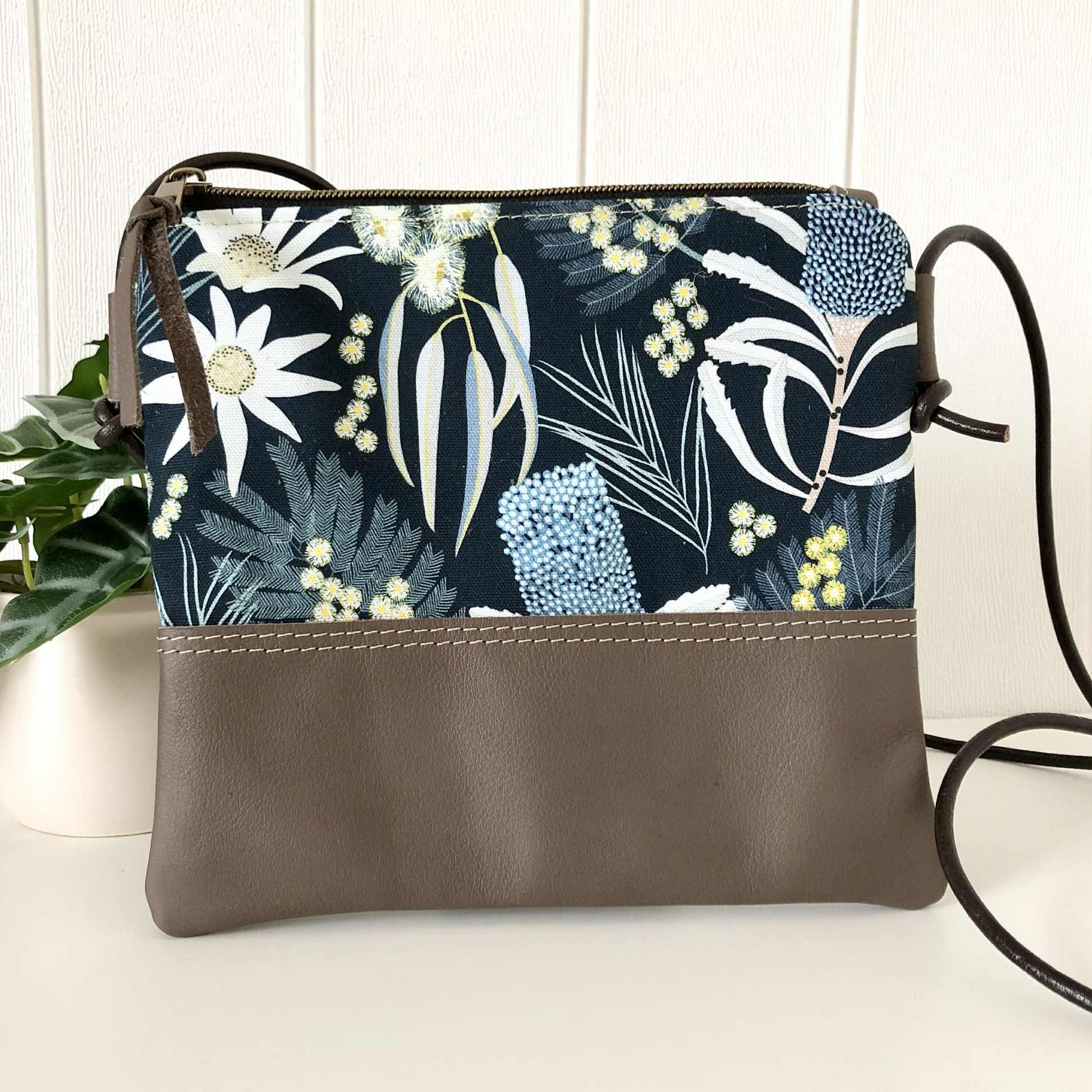 Floral-patterned crossbody bag with brown leather accent on a white surface.